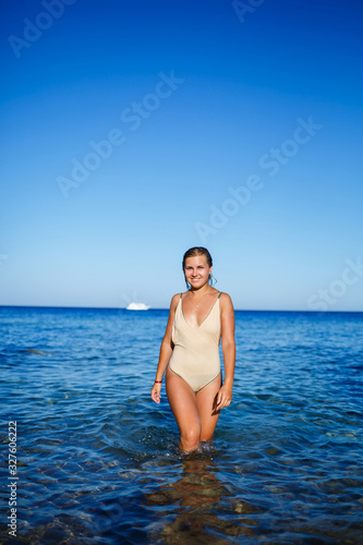 A girl with a beautiful figure in a beige swimsuit in the blue water of the Red Sea. She stands in the bright sun
