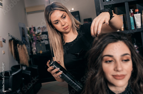Female hairdresser makes hairstyle on young woman with brunette hair in salon.