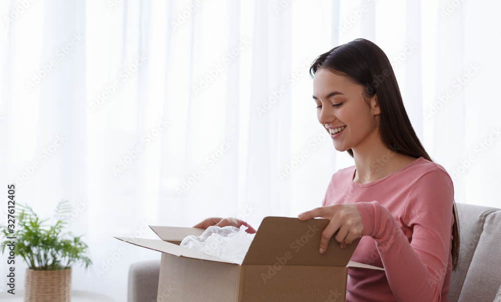 Cheerful girl customer receive and unpacking parcel looking inside Cheerful girl customer receive and unpacking parcel looking inside