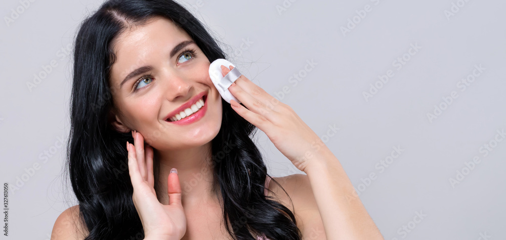 Fototapeta premium Beautiful young woman with makeup kit on a gray background