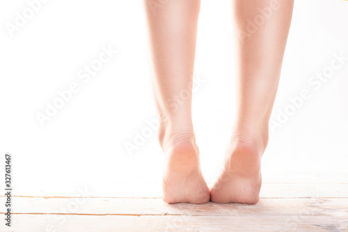 Female, healthy feet, standing on tiptoes on wood floor on a white background. © JacZia