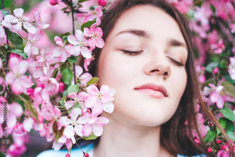 Fototapeta premium Young girl with closed eyes surrounded by flowers of a pink apple tree.