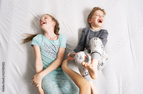 Family time: Dad tickles his children. The girl and boy are lying on the bed and laughing merrily. photo