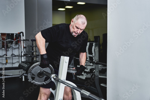 Adult gray-haired man trains on fitness equipment in the gym, pumps legs and arms muscles, loses weight. Concept of healthy lifestyle in old age