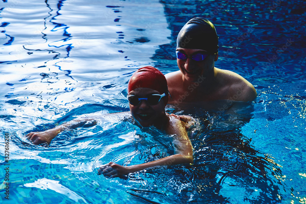 Dad and trainer teaches boy son to swim, have fun, play and splash in a blue swimming pool