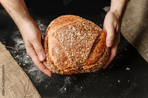 A man holds in his hands a loaf of rustic organic bread.