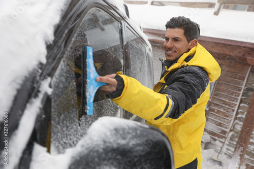 Man cleaning snow from car window outdoors on winter day
