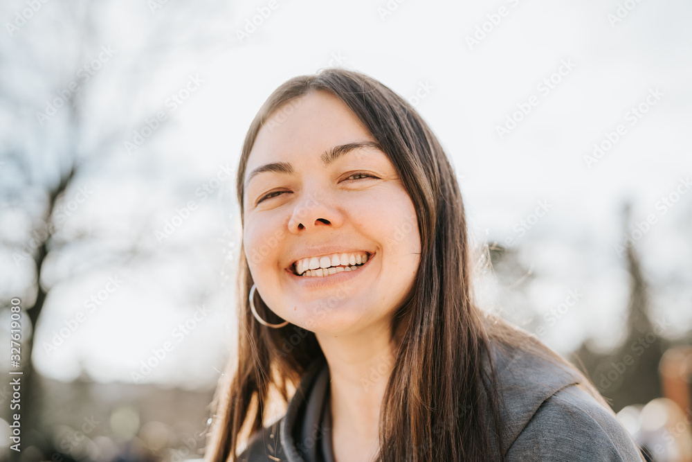 Close up portrait of attractive 40 years old woman looking at camera smiling with toothy smile outdoors. No makeup, natural beauty.