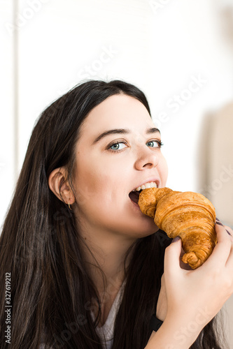 Woman eating croissant.Beautiful straight teeth.Girl is smiling.Baking advertisement.Italian mood.Happy breakfast.Delicious tasty bun. Bakery.Horizontal photo.Place for text.Girl on white background.