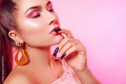 Chic girl with big earrings  accessories on a pink background. Gorgeous pink nude makeup  shiny highlighter.