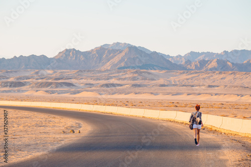 Near East. White girl running away along a wide desert road