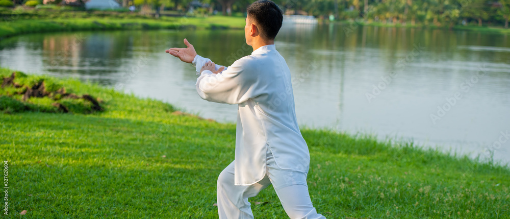 Young man practicing traditional Tai Chi Chuan, Tai Ji and Qi gong in the park for healthy, traditional Chinese martial arts concept. - obrazy, fototapety, plakaty 