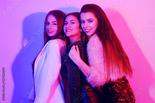Three beautiful girls are dancing in neon. An incredibly fun party with girls in shiny dresses, they celebrate the holiday, smile, laugh, dance, sing. Night club