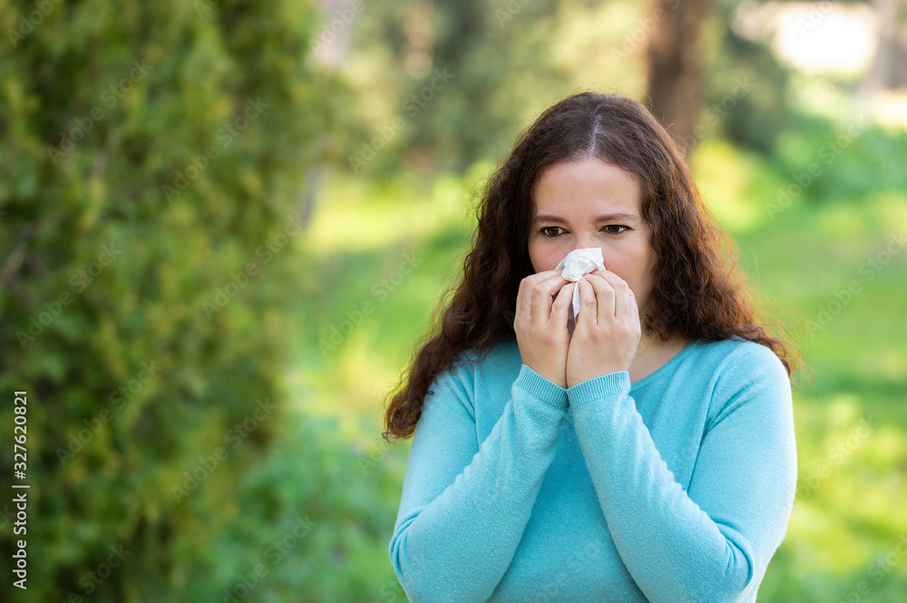 Woman sneezing using a wipe in a park Woman sneezing using a wipe in a park