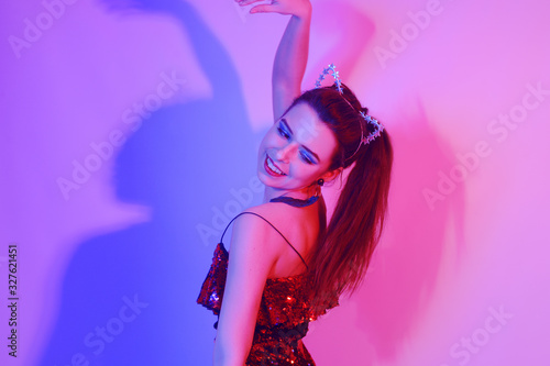 Gorgeous girl dancing in a neon light. A girl in a red shiny dress and with cat ears is dancing