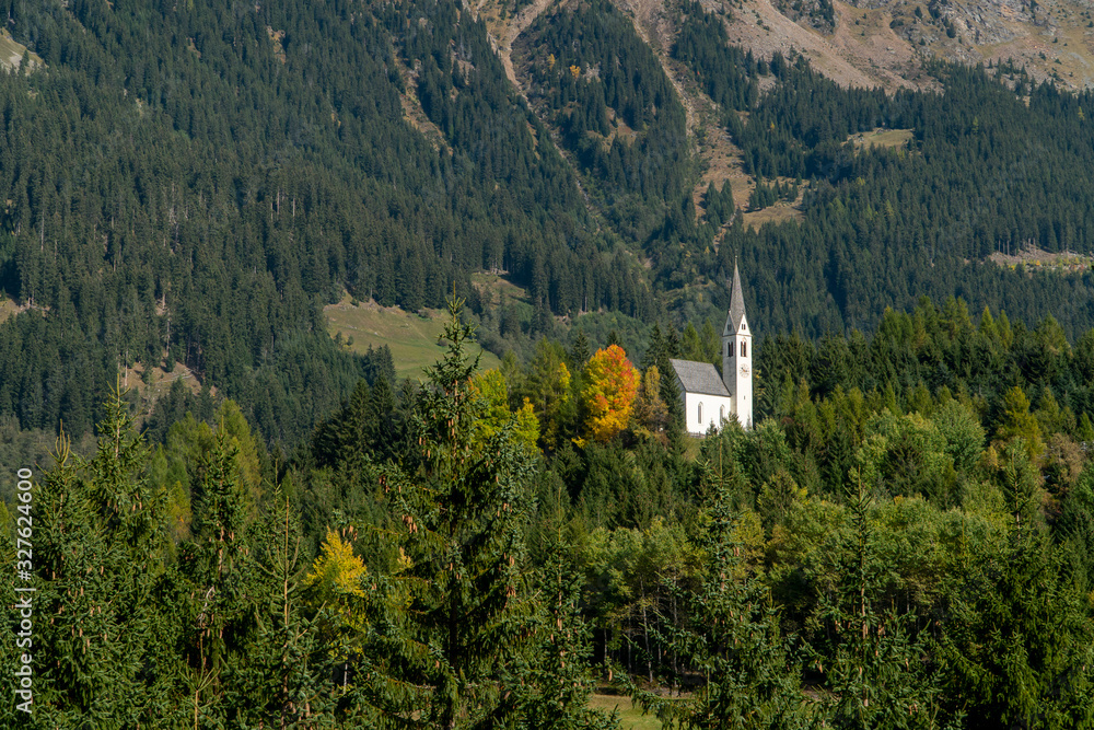 Lonely white church of the Gothic style with a tower and a clock in the forest of Dolomite mountains