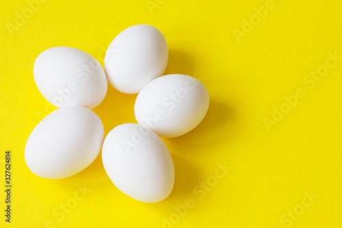 Five white eggs lie on a bright yellow background in the shape of a flower.