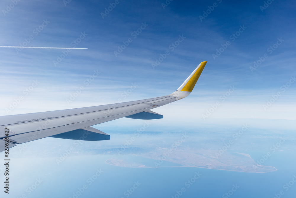 Obraz premium ala de avión de pasajeros airbus a320 sobrevolando el delta del ebro (cataluña, españa), con el cielo zul nublado de fondo.
