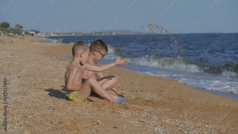 Rest on the sea with children. The boys throw up a shell with sand. Children's emotions. Boys throw sand. Rest on the sea with children. The boys throw up a shell with sand. Children's emotions. Boys throw sand.