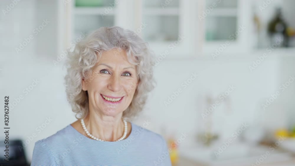 Head and shoulders portrait of beautiful senior woman with curly grey hair looking at camera and smiling happily while posing at home, copy space to right Head and shoulders portrait of beautiful senior woman with curly grey hair looking at camera and smiling happily while posing at home, copy space to right