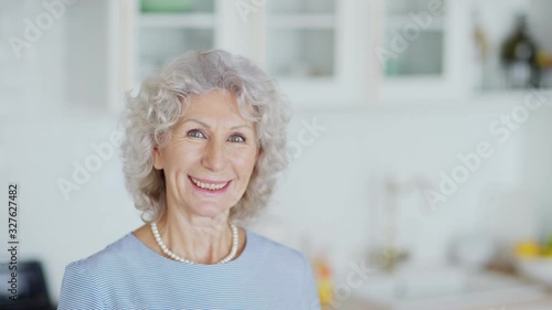 Head and shoulders portrait of beautiful senior woman with curly grey hair looking at camera and smiling happily while posing at home, copy space to right photo