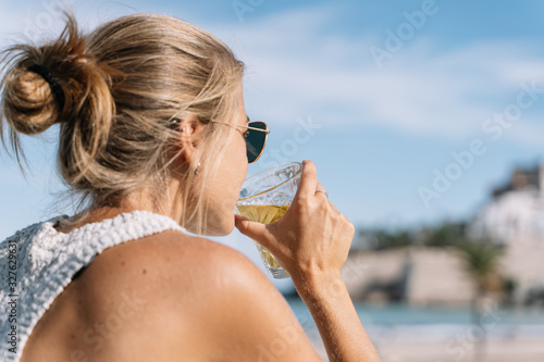 Blonde girl with her hair up and sunglasses drinking a beer