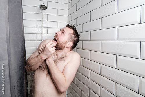 Fotografia Shocked man looks at a watering can in the shower room, from which, unexpectedly, cold water is pouring