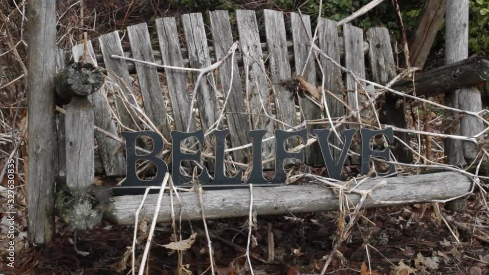 A dreary cedar swing with the word BELIEVE resting upon dead vines A dreary cedar swing with the word BELIEVE resting upon dead vines