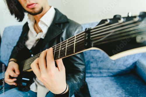 Young man practicing with his electric guitar on the sofa of his house learning.