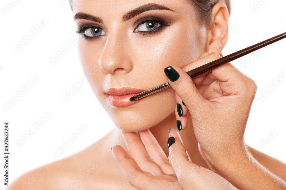Make-up artist does lips make-up to a woman with smoky eyes makeup. Beautiful portrait of a girl close up. Professional makeup and cosmetology skin care. Make-up artist does lips make-up to a woman with smoky eyes makeup. Beautiful portrait of a girl close up. Professional makeup and cosmetology skin care.