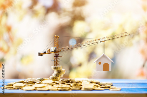 Stacking gold coins with increase and tower crane and hoist brake solutions with build new house in the public park, saving money and loan for construction real estate and home concept.