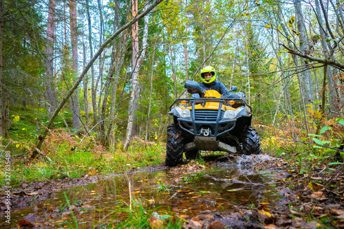A man riding an ATV off-road. A large puddle in front of the ATV. Biker rides through the woods. Extreme off-road racing. Quad bike on the background of the forest. All terrain vehicle