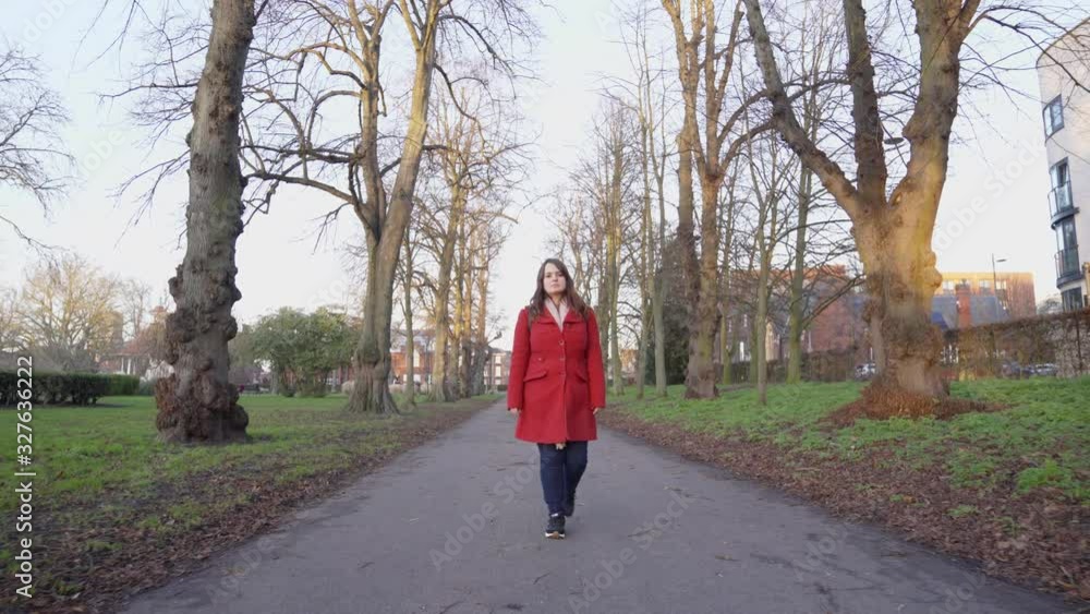 Woman in a red coat, walking through a pathway in a park, during winter season. Woman in a red coat, walking through a pathway in a park, during winter season.