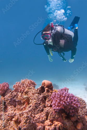 Young diver swimming in blue sea with coral