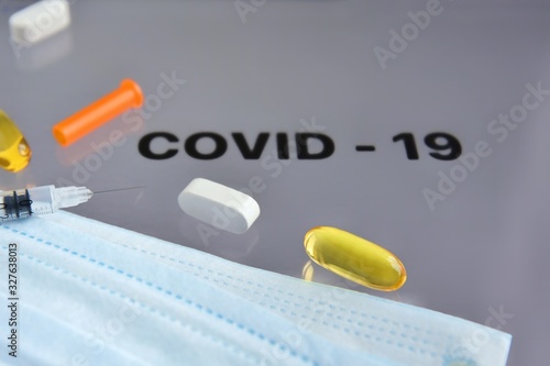 Inscription COVID-19 on display with pills, syringe, thermometer and protection mask on background. Dangerous asian ncov corona virus, dna, pandemic risk background design