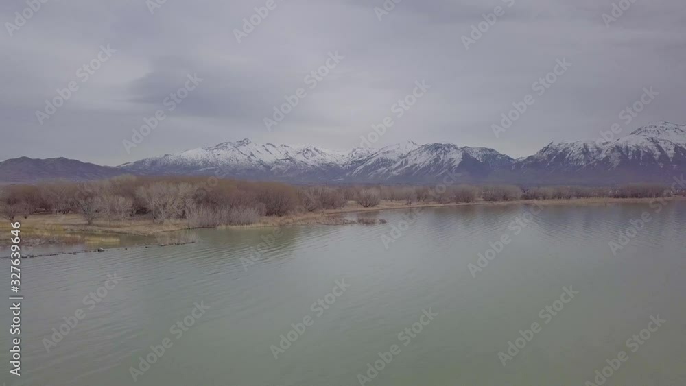 Aerial view of a large lake with snow-capped mountains in the distance - slide and pan motion results in parallax effect