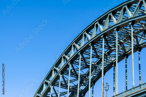 A portion of the Tyne Bridge, at a dynamic angle, featured at the bottom right hand section of the image contrasting against a beautiful blue sky.