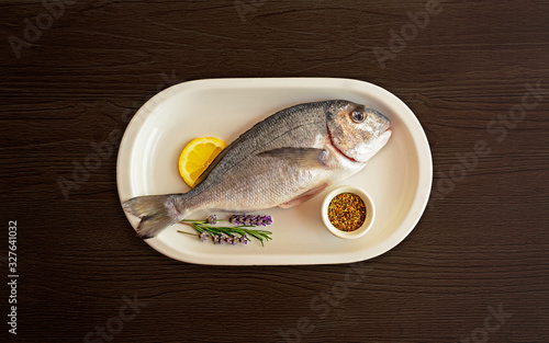 The concept of simple and healthy food. The Mediterranean diet and its dish. Fresh, peeled Dorado with lemon, lavender and spices prepared for cooking on a dark wooden background. Food photo
