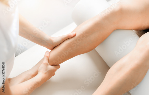 Professional therapist giving relaxing leg massage treatment to athlete woman in therapy centre.