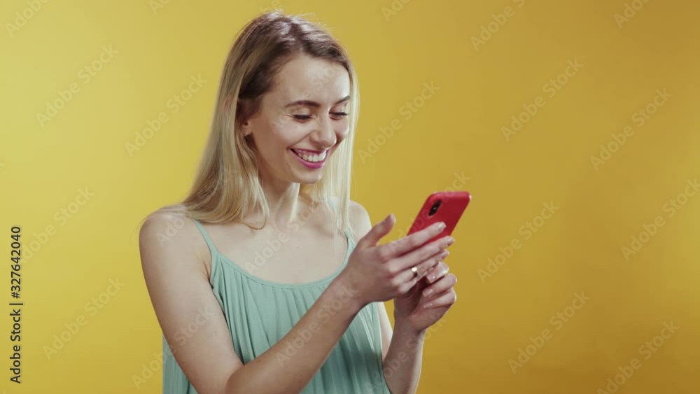 People and technology. Modern young woman using a smartphone typing message in social media laughing communicating posing at orange background. People and technology. Modern young woman using a smartphone typing message in social media laughing communicating posing at orange background.