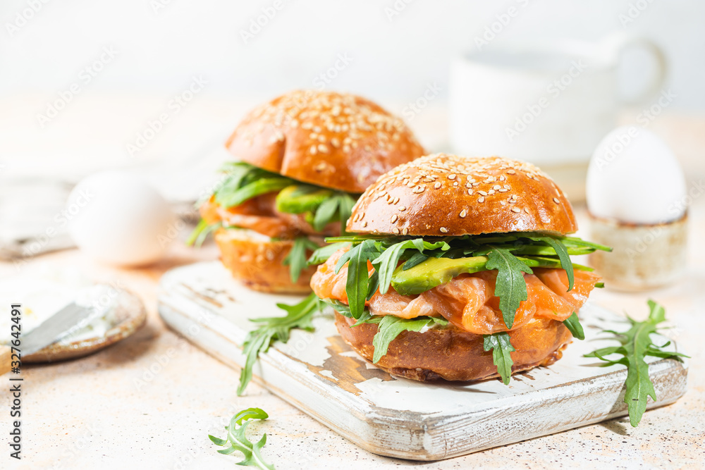 Burger sandwich with salmon, cream cheese, avocado and arugula on a light background, concept diet food, take away, healthy fast food Burger sandwich with salmon, cream cheese, avocado and arugula on a light background, concept diet food, take away, healthy fast food