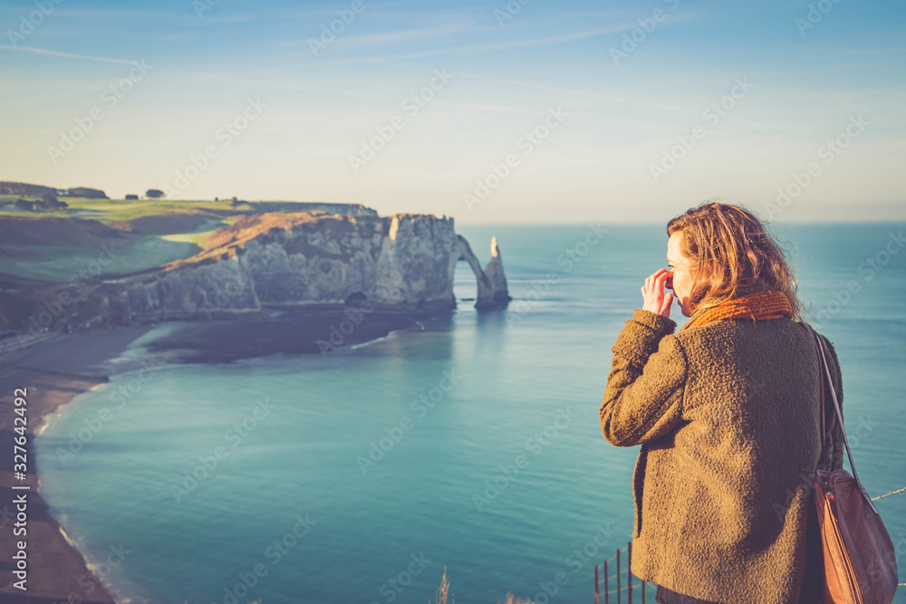 tourist girl woman visiting the coastal landscape along the Falaise d'Aval the famous white cliffs of Etretat village with the Porte d'Aval natural arch and the rock known as the Aiguille d'Etretat
