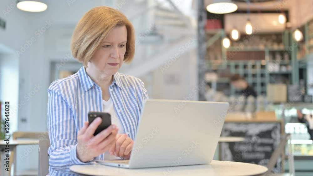 Smartphone use by Creative Old Woman with Laptop in Cafe Smartphone use by Creative Old Woman with Laptop in Cafe