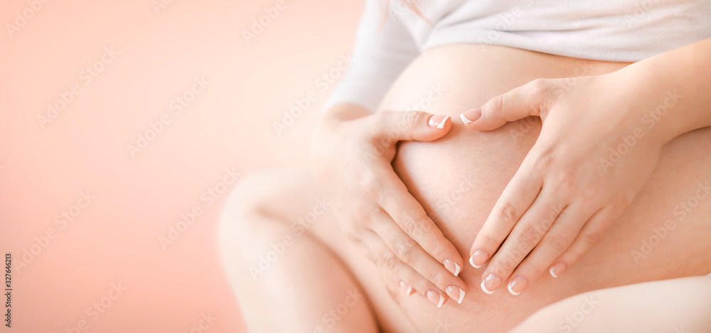 Pregnant woman belly detail isolated on pink Background. Pregnancy tummy concept wide banner or copy space for text.