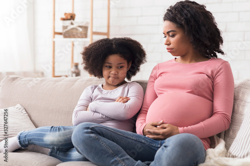 Wall Mural Upset little daughter looking at her pregnant mother's belly with jealousy