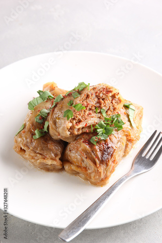The concept of Eastern European cuisine. Stuffed cabbage with meat, rice and herbs on a light plate on a light background. Background image, copy space