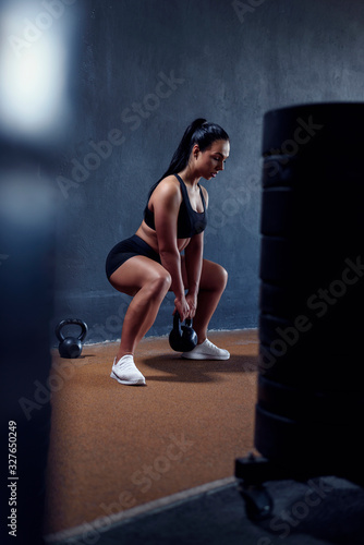 Woman fitness model make workout with weights - squat with kettlebell. Tanned sporty female  with athletic figure. Vertical portrait of sportswoman.