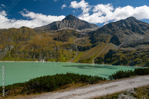 A view of the Alpine dam at the foot of the rocky peaks under the blue sky with nice clouds