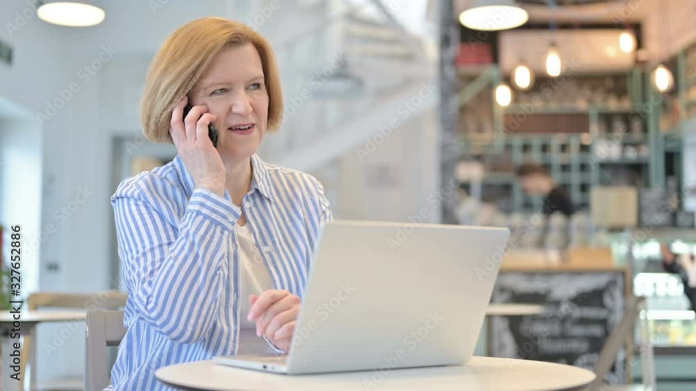 Creative Old Woman with Laptop Talking on Smartphone in Cafe Creative Old Woman with Laptop Talking on Smartphone in Cafe