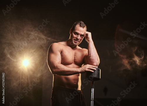Bodybuilder leaning on the barbell in a thinking pose surrounded by smoke looking questioned